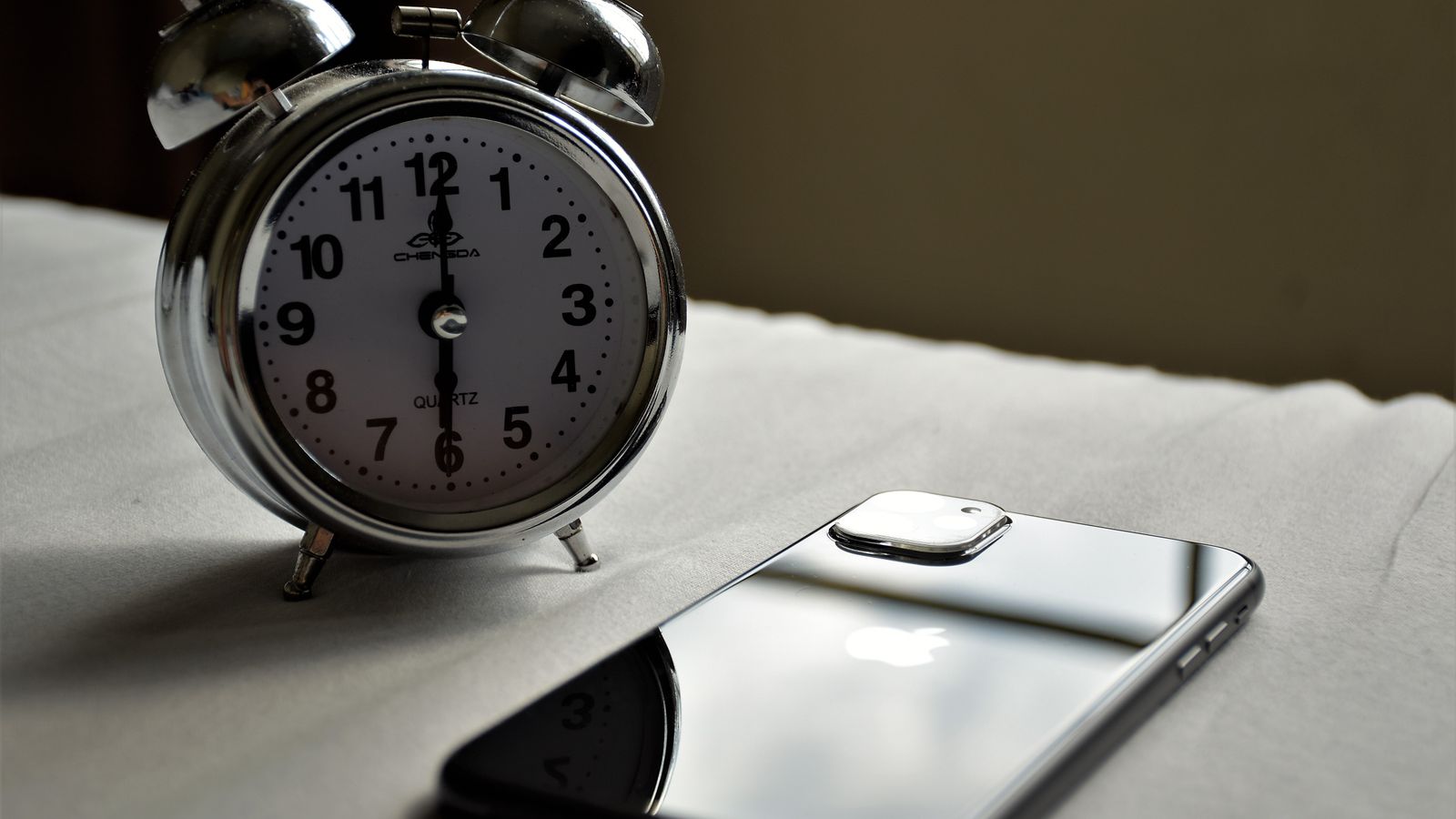 A silver alarm clock and a smartphone placed side by side