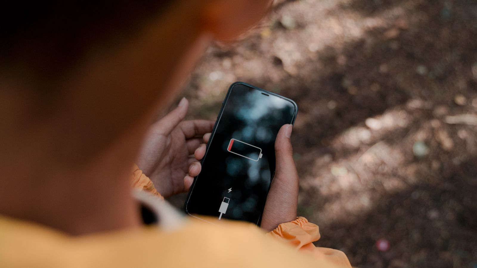 Teenager with a low-battery smartphone alone in a forest, evoking solitude and disconnection