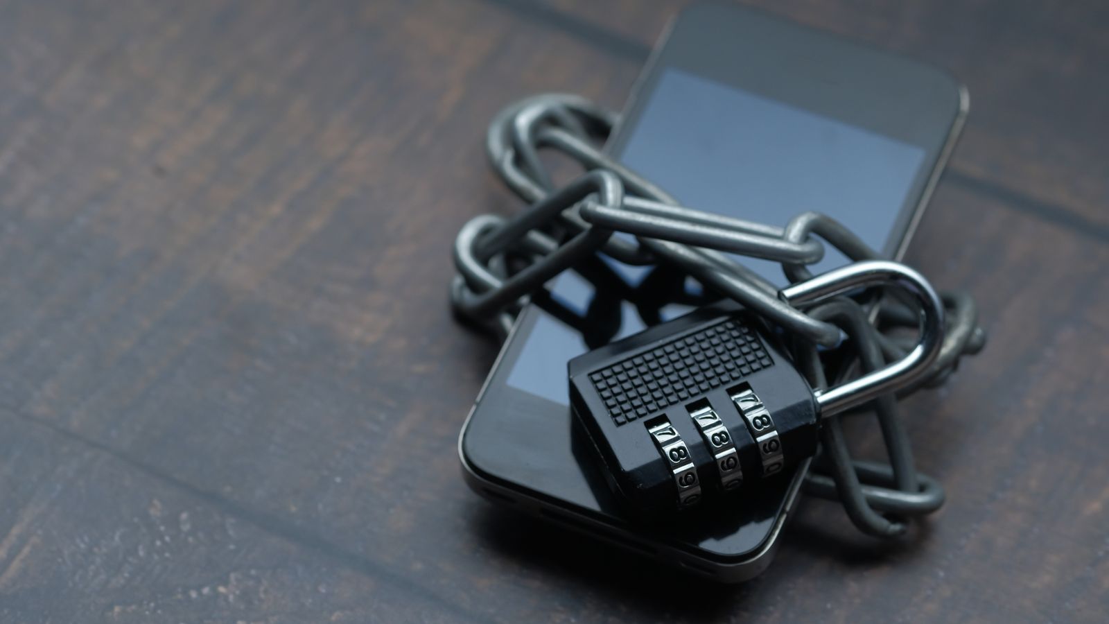Close-up of a smartphone wrapped in a chain with a padlock, symbolizing a blocked app