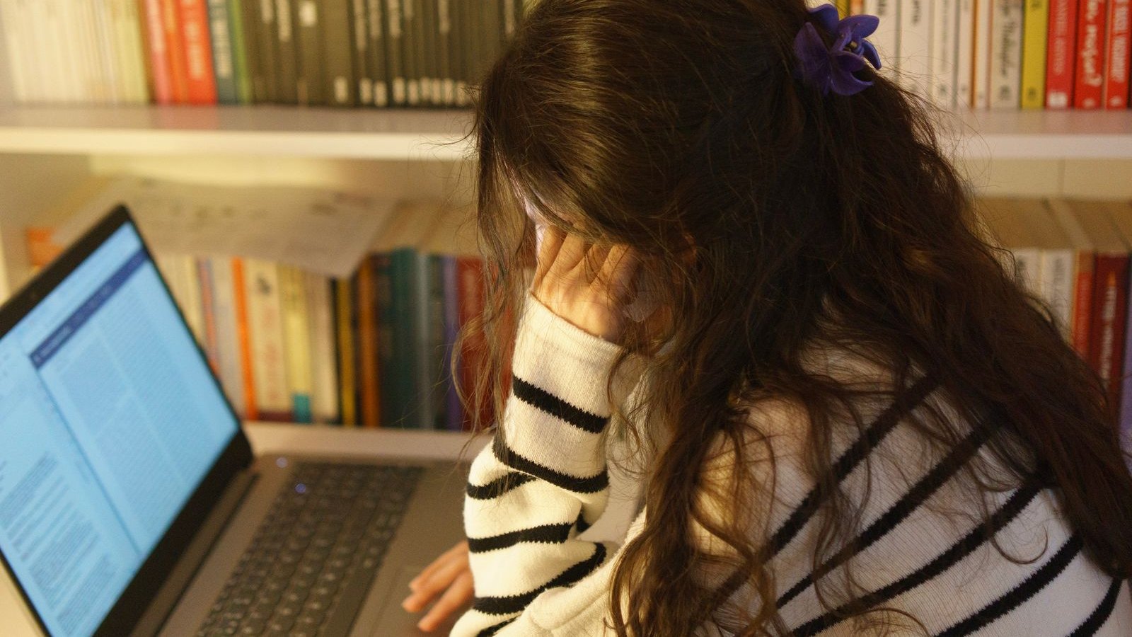 Student studying with a laptop in a library, looking stressed