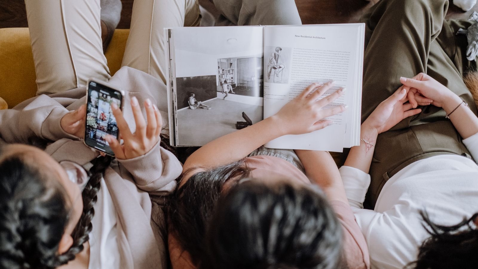 People sitting on a couch, one holding a phone and one holding a book