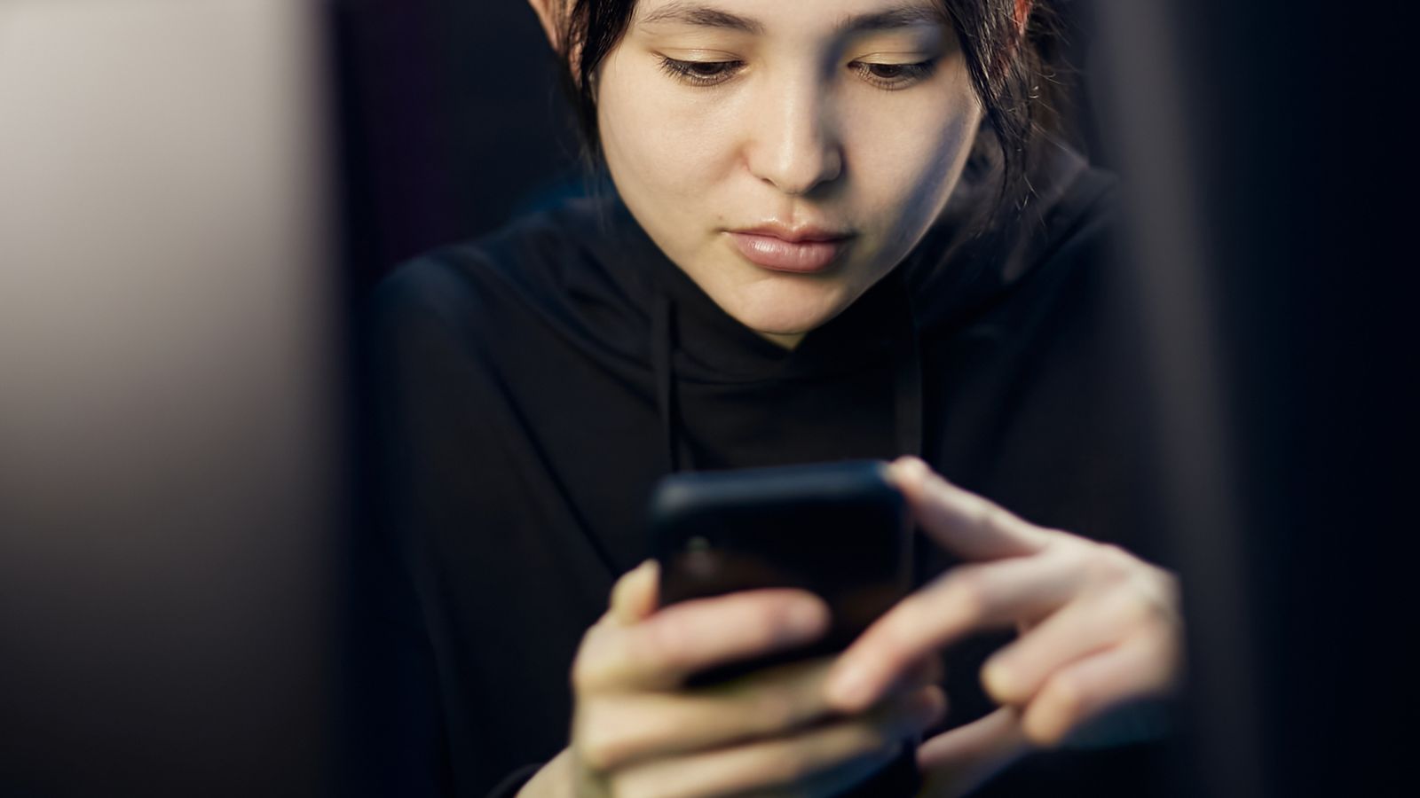 Woman intently looking at her smartphone indoors in dim lighting