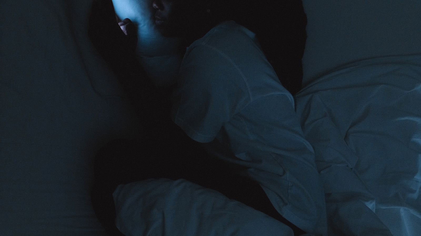 Woman lying in bed at night scrolling on her phone in a dark room