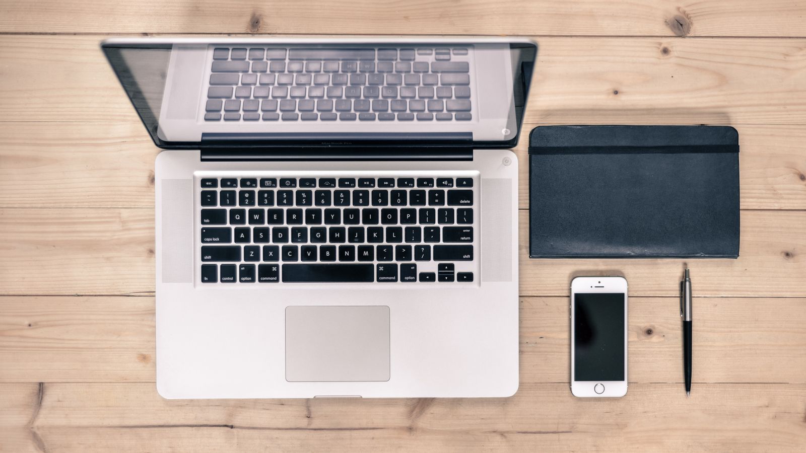 Top view of a tidy workspace with a laptop, smartphone, notebook, and pen on a wooden desk