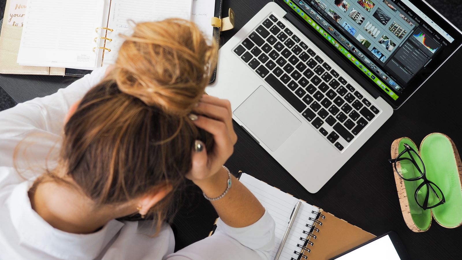 Overhead view of a stressed woman working at a desk with a laptop and phone