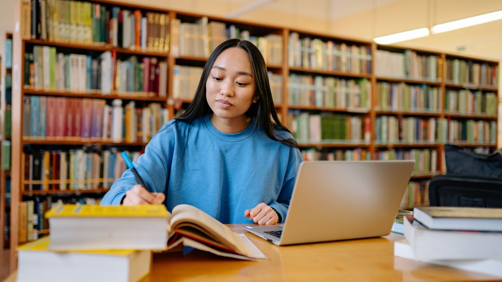 Young woman studying in a library with books and a laptop